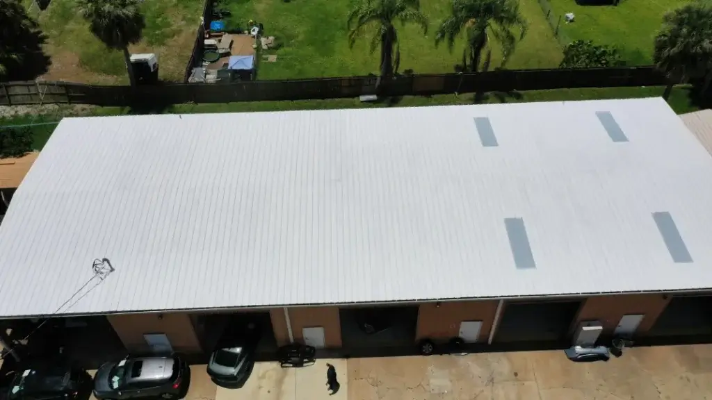Aerial view of a large commercial building with a white metal roof featuring rectangular skylights