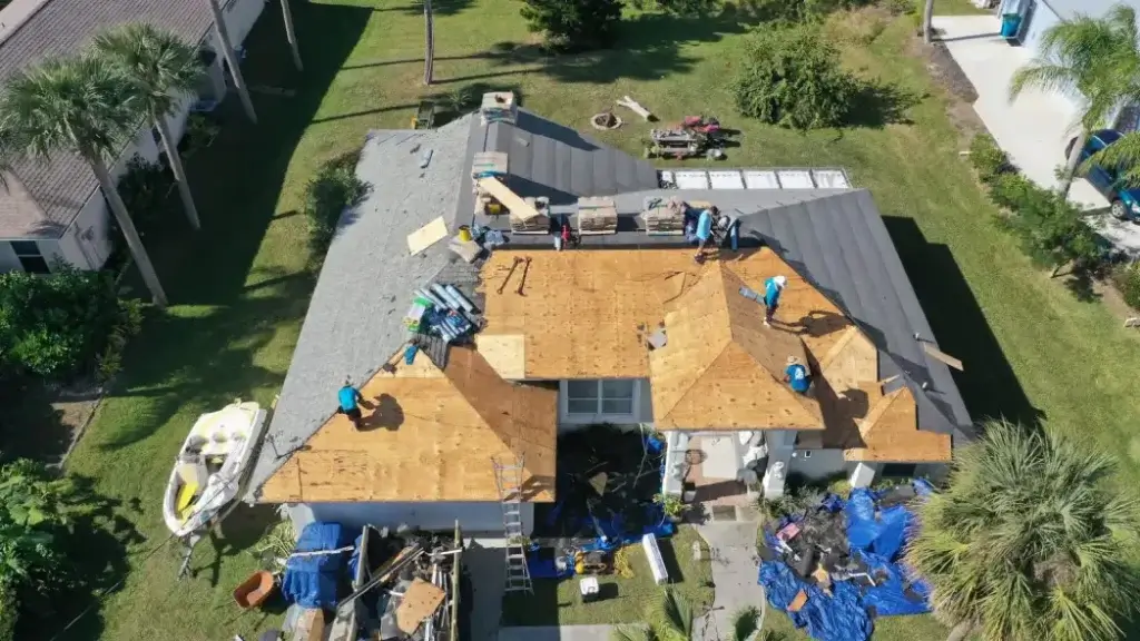 Aerial view of a residential house undergoing storm damage roof repair with construction workers installing new roofing materials.
