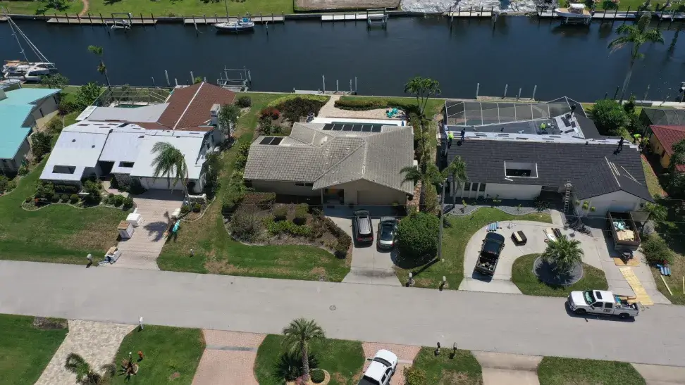 Aerial view of a residential area with homes beside a waterway, featuring manicured lawns, driveways with cars, and multiple docks with detailed roofing.