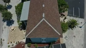 Aerial view of a building with a triangular-shaped roof, featuring new gutter replacement, and surrounding palm trees.
